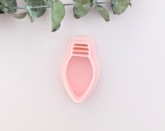May include: A pink plastic cookie cutter shaped like a light bulb. The cutter has a double layer design.