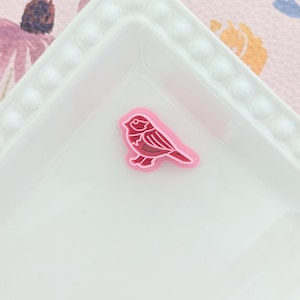 May include: A pink plastic bird-shaped cookie cutter on a white plate with a floral pattern.