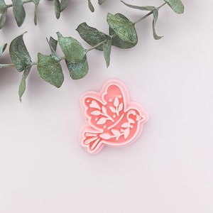 May include: Pink plastic cookie cutter shaped like a dove with floral details.