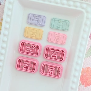 Op de afbeelding: Een verzameling rechthoekige koekjesvormen en bijpassende reliëfstempels in pastelkleuren. De stempels bevatten boekgerelateerde teksten zoals Just One More Chapter, Book Trope, Spicy en Romance Reader Club, elk met een klein boekicoontje.