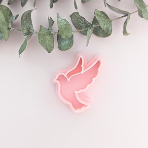 May include: A pink plastic dove-shaped cookie cutter on a white background.