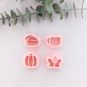 May include: Four pink plastic cookie cutters shaped like a pumpkin, a pie slice, a coffee mug, and a leaf.