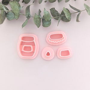 Op de afbeelding: Een set van vier roze plastic koekjesuitstekers in de vorm van een pot, een deksel, een driehoek en een rechthoek.