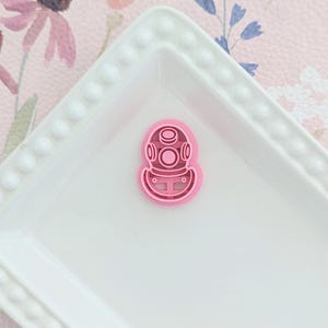 May include: Pink plastic cookie cutter shaped like a scuba diving helmet.