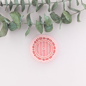 May include: A pink plastic cookie cutter shaped like a round door with a brown wooden door and a small round knob.