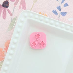 Op de afbeelding: Roze siliconen mal met drie spookvormen. De mal ligt op een wit bord met een geperlde rand.