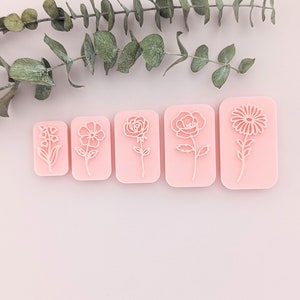 May include: Five pink rubber stamps featuring various flower designs. The stamps are arranged in a line from left to right, with the smallest stamp on the left and the largest stamp on the right.