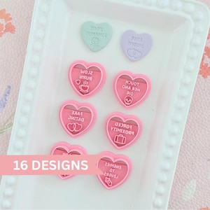 Peut inclure: Une collection d'emporte-pièces en forme de cœur en rose, vert clair et violet clair. Les emporte-pièces présentent du texte en relief, notamment "Dark Romance", "Fake Dating", "Slow Burn", "Touch Her And Die", "Forced Proximity" et "Enemies To Lovers".