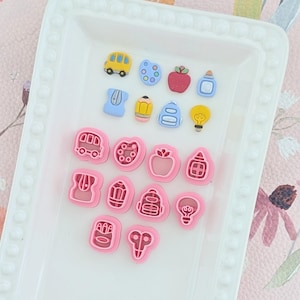 May include: A collection of school-themed craft supplies, including a yellow school bus, red apple, and pencil-shaped items. The items are in various colors and shapes, perfect for crafting projects. The items are arranged on a white tray.