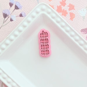 Peut inclure: Un emporte-pièce en forme de pile de citrouilles en plastique rose sur une assiette blanche avec un fond à motif floral.