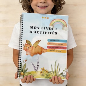 Peut inclure: Un cahier d'activités à spirales avec le titre "MON LIVRET D'ACTIVITÉS". La couverture présente un dragon de dessin animé, un arc-en-ciel et des étiquettes de sujets. Le livre est tenu par une personne.