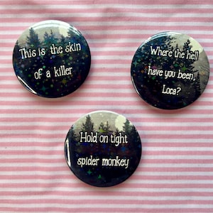 May include: Three round black and white buttons with a forest scene and glitter. The text on the buttons reads "This is the skin of a killer", "Where the hell have you been, Loca?" and "Hold on tight spider monkey".