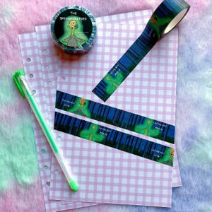 May include: Decorative tape roll and strips with a cartoon character and the text "I bring you peace" on a blue and green background. A green pen and pink checkered paper are also visible in the image.