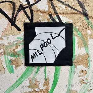 May include: A square black patch with the words "MIL POOL" in white, stylized text. The patch features a white graphic of a basketball. The patch is on a textured wall with graffiti.