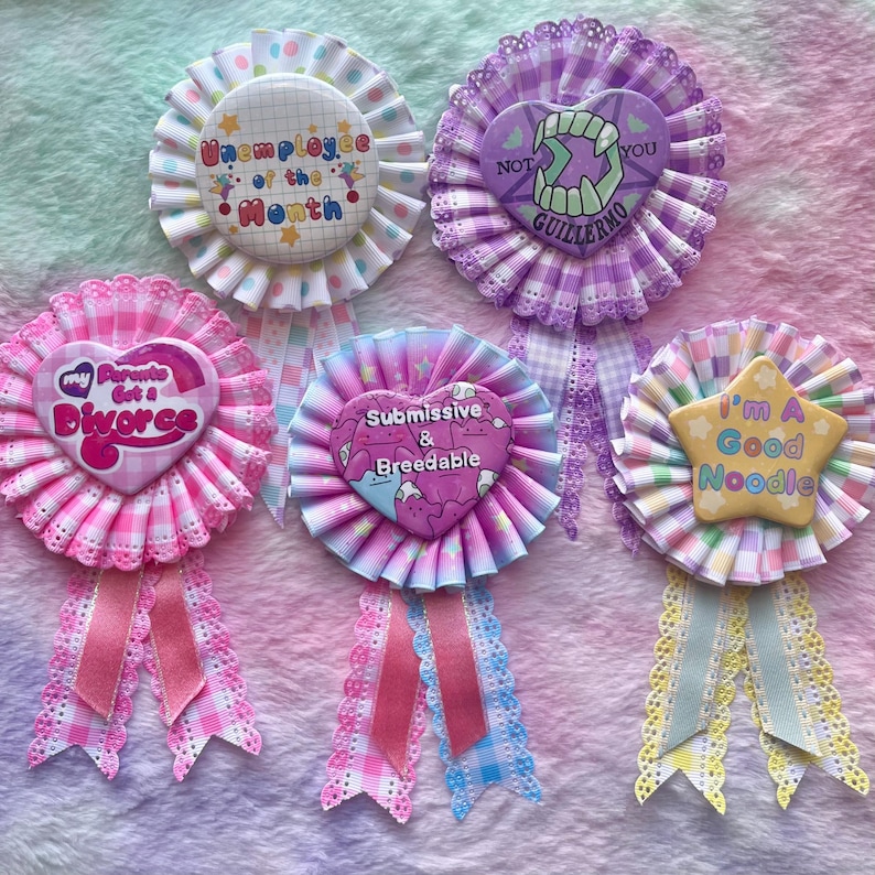 May include: Five colorful fabric rosettes with different pins attached. The pins feature various designs and text, including "Unemployee of the Month", "My Parents Got a Divorce", "Submissive & Breedable", "Not You Guillermo", and "I'm a Good Noodle".
