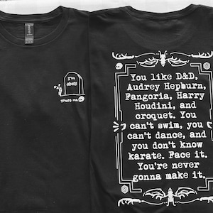 May include: Black t-shirts with white graphics. One shirt features a tombstone with the text "I'm okay" and "Trust me." The other shirt has a quote about D&D, Audrey Hepburn, and other interests.