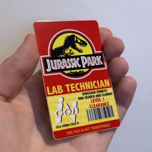 Peut inclure: Un badge d'identification rectangulaire de technicien de laboratoire Jurassic Park. La partie supérieure est rouge avec le logo Jurassic Park. Le bas est jaune avec le texte "Lab Technician", "Dinosaur Embryo DNA Search and Cloning" et "Level 1 Clearance".