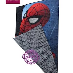 Puede incluir: Una alfombra azul y roja con una imagen de dibujos animados de la cara de Spiderman. La alfombra tiene un patr&oacute;n geom&eacute;trico en blanco y negro en la parte posterior.