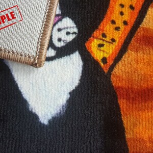 Pu&ograve; includere: Primo piano di un tappeto colorato con un design di animali in bianco e nero. Il tappeto ha un bordo marrone e un timbro rosso "SAMPLE" nell'angolo in alto a sinistra.