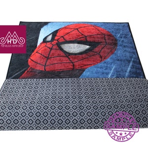 Puede incluir: Una alfombra roja y azul con una imagen de dibujos animados de la cara de Spiderman. La alfombra tiene un patr&oacute;n de diamantes grises y negros en la parte posterior.