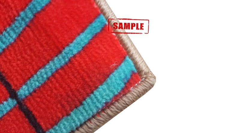 Pu&ograve; includere: Primo piano del bordo di un tappeto a strisce rosse e turchesi con un bordo beige. Il tappeto ha una trama tessuta ed &egrave; etichettato "SAMPLE".
