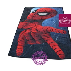 Puede incluir: Una alfombra de Spiderman roja y azul con fondo negro. La alfombra presenta una imagen de primer plano de la cara y la mano de Spiderman. La alfombra tiene un sello "SAMPLE" en la esquina inferior derecha.