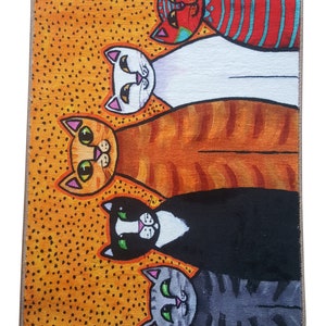Pu&ograve; includere: Un tappeto colorato con un design di cinque gatti in fila. I gatti sono tutti di colori diversi e hanno diversi motivi sulla loro pelliccia. Lo sfondo del tappeto &egrave; di un arancione brillante con punti neri.