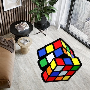 以下が含まれることがあります： カラフルな3Dプリントの敷物で、ルービックキューブが描かれています。敷物は、モダンなリビングルームの薄いグレーのタイル張りの床の上にあります。