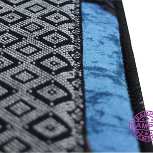 Puede incluir: Primer plano de una tela con estampado en blanco y negro con un borde de tela azul. La tela tiene un dise&ntilde;o geom&eacute;trico con peque&ntilde;os puntos blancos. El borde es de color azul s&oacute;lido. La palabra "SAMPLE" est&aacute; estampada en morado en la tela azul.