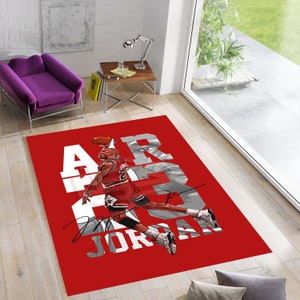Puede incluir: Alfombra roja y blanca con un gráfico de un jugador de baloncesto en el aire, con el texto "AIR JORDAN" en letras blancas.