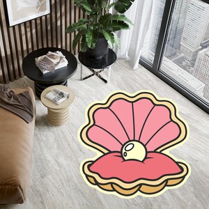 Könnte beinhalten: Ein rosa-gelber Cartoon-Muschelteppich mit einer Perle darin. Der Teppich liegt auf einem hellgrauen Boden.