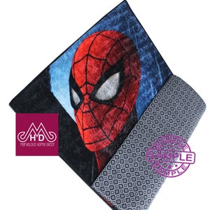 Puede incluir: Una alfombra roja y azul con una imagen de primer plano de la cara de Spider-Man. La alfombra tiene un patr&oacute;n geom&eacute;trico blanco y negro en el borde inferior. La alfombra est&aacute; etiquetada como "Marvelous Home Decor" y "Sample".