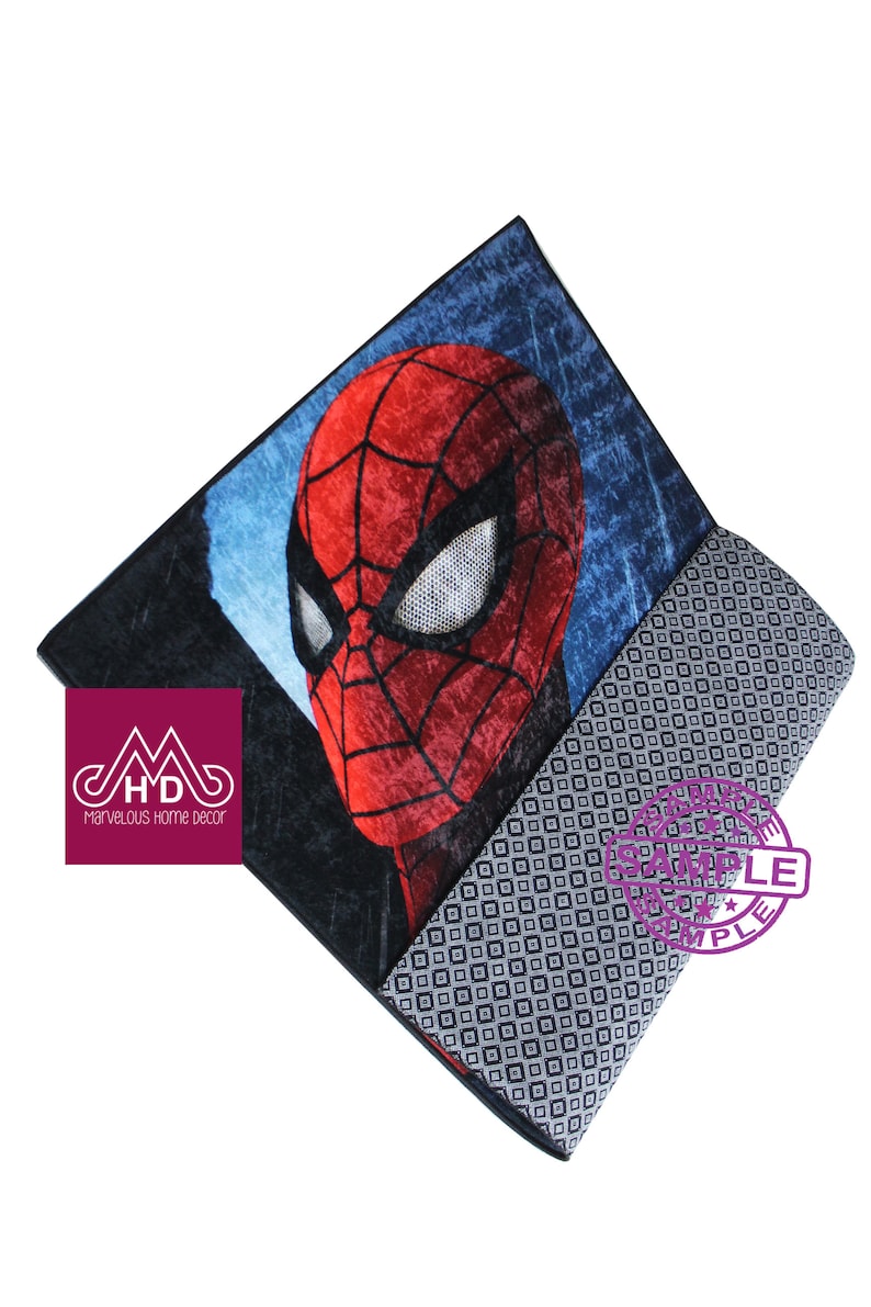 Puede incluir: Una alfombra roja y azul con una imagen de primer plano de la cara de Spider-Man. La alfombra tiene un patr&oacute;n geom&eacute;trico blanco y negro en el borde inferior. La alfombra est&aacute; etiquetada como "Marvelous Home Decor" y "Sample".