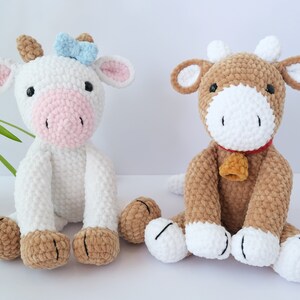 May include: Two crocheted plush cow toys. One is white with a pink nose and a blue bow. The other is brown with a white nose and a red bell.