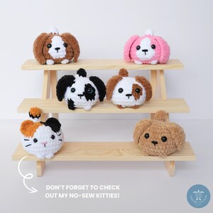 Pu&ograve; includere: Cinque animali di peluche all'uncinetto, tra cui un gatto e quattro cani, sono esposti su uno scaffale di legno. Gli animali sono tutti di colori diversi e hanno espressioni facciali diverse. Lo scaffale &egrave; in legno e ha tre livelli. Il testo "DON'T FORGET TO CHECK OUT MY NO-SEW KITTIES!" &egrave; scritto sotto lo scaffale.