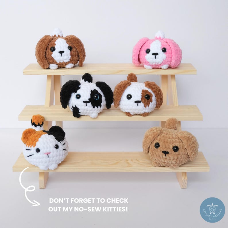 Pu&ograve; includere: Cinque animali di peluche all'uncinetto, tra cui un gatto e quattro cani, sono esposti su uno scaffale di legno. Gli animali sono tutti di colori diversi e hanno espressioni facciali diverse. Lo scaffale &egrave; in legno e ha tre livelli. Il testo "DON'T FORGET TO CHECK OUT MY NO-SEW KITTIES!" &egrave; scritto sotto lo scaffale.