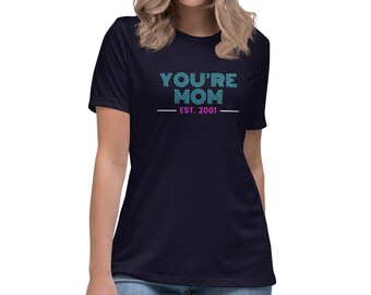 May include: Navy blue t-shirt with the text "YOU'RE MOM EST. 2001" in teal. The text is centered on the front of the shirt. The shirt has a relaxed fit and short sleeves.