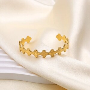 May include: A gold-toned bracelet featuring a delicate design of interlocking four-leaf clover shapes.
