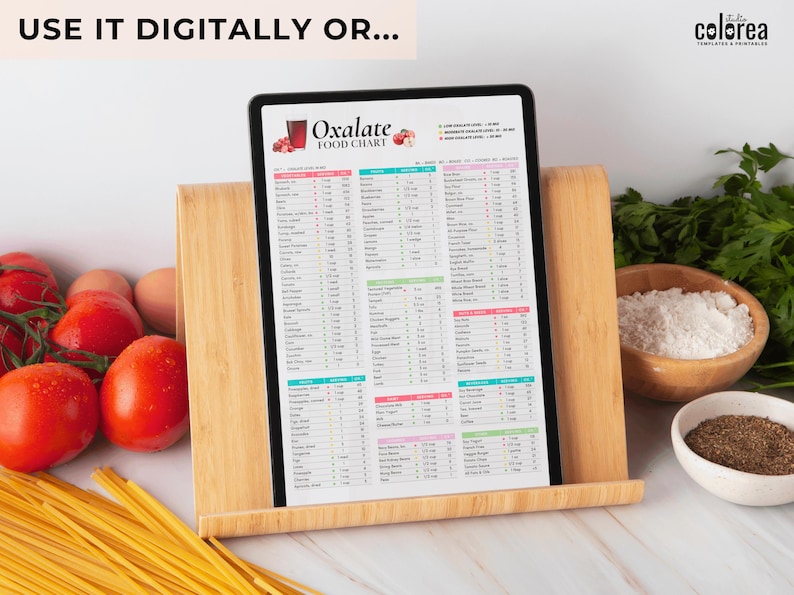 Puede incluir: Un gr&aacute;fico digital imprimible titulado "Oxalate Food Chart" con una lista de alimentos y su contenido de oxalato. El gr&aacute;fico se muestra en una tableta apoyada en un soporte de madera. Hay tomates, pasta y un taz&oacute;n de harina en el fondo.