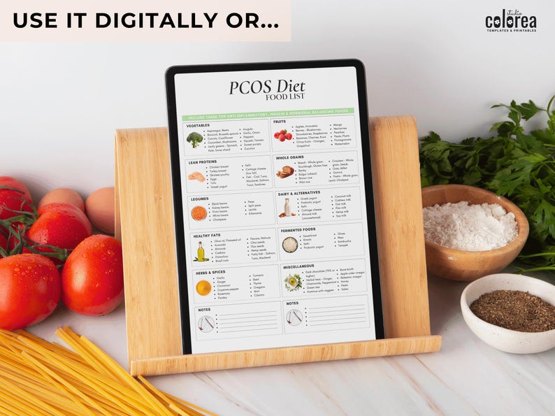 May include: A printable PCOS diet food list on a tablet propped up on a wooden stand. The list includes categories for vegetables, lean proteins, legumes, healthy fats, herbs & spices, fruits, whole grains, dairy & alternatives, fermented foods, and miscellaneous. The tablet is surrounded by various food items, including tomatoes, pasta, rice, and spices.