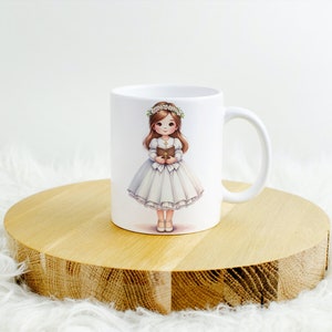 May include: White ceramic mug with a colorful illustration of a girl in a white dress and a flower crown holding a book. The girl is standing on a wooden surface.