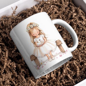May include: White ceramic mug with a colorful illustration of a girl wearing a white dress and a flower crown, holding a book and sitting on a wooden bench. The girl has long blonde hair and blue eyes. The mug has a handle on the right side.