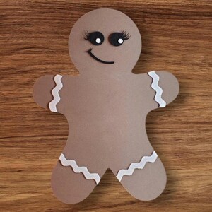 May include: A brown gingerbread person cutout with white icing and black eyes. The gingerbread person is smiling.
