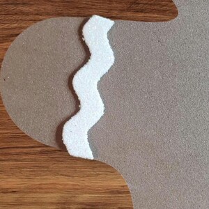 May include: A white, glittery, zig-zag trim on a brown background. The trim is a decorative element for a craft project.