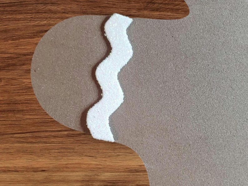 May include: A white, glittery, zig-zag trim on a brown background. The trim is a decorative element for a craft project.