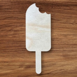 Puede incluir: Un recorte de madera con forma de paleta, con una mordida en la parte superior. El recorte es de color claro y tiene un mango. El fondo es una superficie de madera marrón.