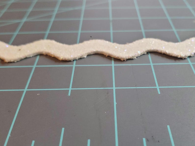 May include: White glitter trim with a wavy edge.