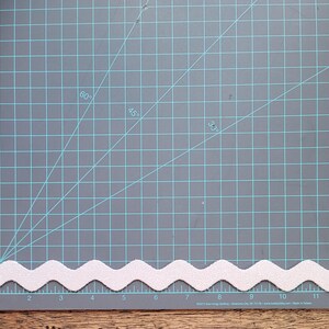 May include: White zig zag trim on a gray cutting mat with a grid pattern. The trim is about 12 inches long.