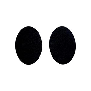 May include: Two black, oval-shaped earrings on a white backdrop. The earrings have a textured surface and a simple, minimalist design. They are likely made of a dark material, possibly leather or a similar fabric.