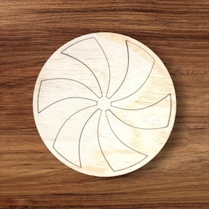 Op de afbeelding: Een ronde houten schijf met een gesneden swirl-ontwerp. De schijf is lichtbruin en het swirl-ontwerp is donkerbruin.